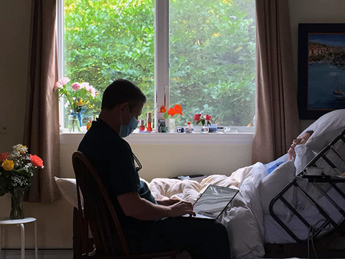 Care Dimensions RN Case Manager Rick Healy enters notes at the bedside of patient Joëlle Birkett. (Photo courtesy of Bob Birkett)