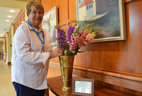 Community volunteer Kathe Hyland displays one of her floral arrangements in a brass vase at Care Dimensions' Kaplan Family Hospice House. Kathe volunteers as a way to give back for the care her mother received at the hospice house.