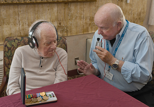 Care Dimensions veteran-to-veteran volunteer Jerry Dunn shares stories with his patient, John Graham, a WWII veteran who wears a hearing amplifier that Jerry bought for him.