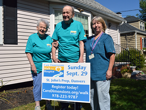 Care Dimensions Hospice Aide Dale Lemure (right) poses with Marge and Frank Walker of Salem, MA by a Walk for Hospice sign in the Walkers' yard in 2019.