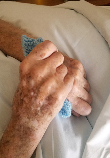 hospice patient hand grasping prayer square knitted by Care Dimensions volunteer