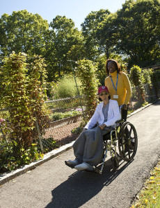 Care Dimensions volunteer pushing hospice patient in wheelchair by garden