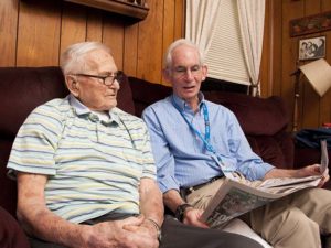 Care Dimensions volunteer Jeff Brand (right), an Air Force veteran from Marblehead, reviews the newspaper sports section with Stanley Lojko, a World War II Army veteran and hospice patient from Salem.