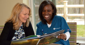 Care Dimensions hospice aide Guerline Dorvelus shares a book with a female patient