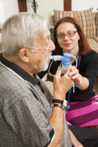 Susan Powers, Care Dimensions hospice and palliative care nurse practitioner, assists respiratory patient Tom DeVeau with a nebulizer.